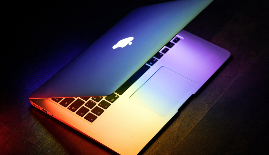 Photo of a half open MacBook under colourful lights